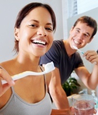 Man and woman with dental implants brushing teeth