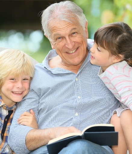 Grandfather enjoying the benefits of dental implants and smiling with grandchildren