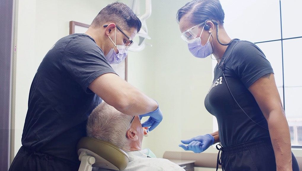 Dentist and dental team member examining patient's smile in treatment room