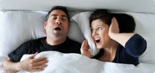 Frustrated woman in bed with snoring man who need sleep apnea therapy