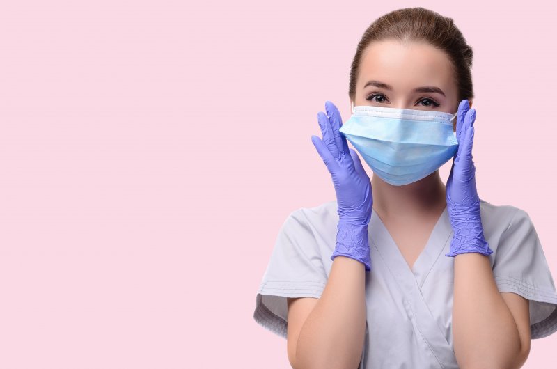 a female dentist wearing gloves, scrubs, and a face mask 