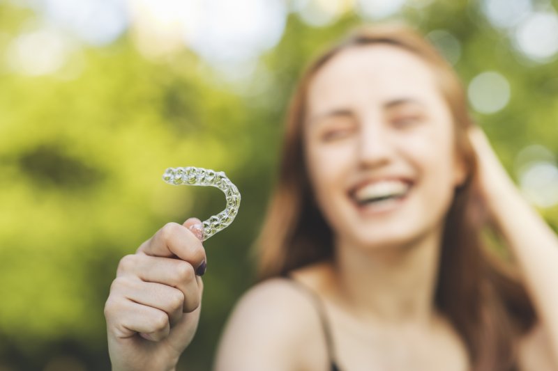 young woman smiling while holding Invisalign aligner